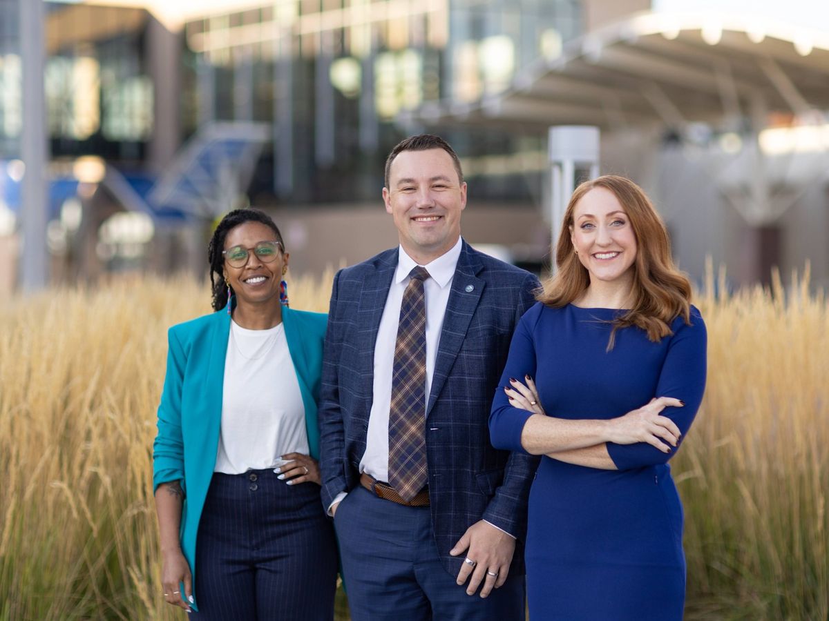 Erik Muckey, June CopperStad and Kadyn Wittman smiling in front of tall prairie grass downtown
